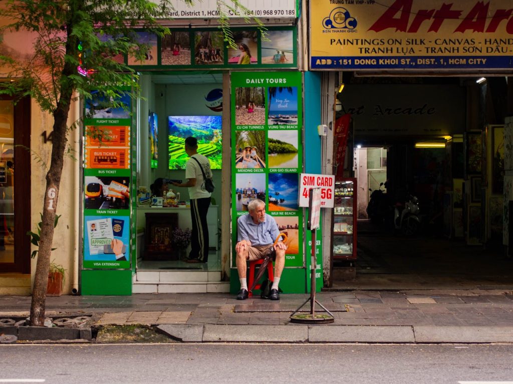 A senior man sitting outside a bustling tour office in Ho Chi Minh City, Vietnam.